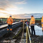 Wide hero editorial photograph of a major UK growth corridor taking shape at sunrise, showing a mixed team of civil