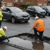 Highways professionals inspect rain-damaged asphalt beside a suburban road
