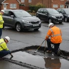 Highways professionals inspect rain-damaged asphalt beside a suburban road