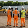 Civil engineering team surveys ground beside excavator and restricted access route