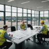 Engineering professionals review pavement plans overlooking a busy logistics yard