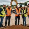 Three groundworks professionals inspect soil conditions at a British construction site
