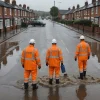 Engineers assess overwhelmed drainage on a rain-soaked British street